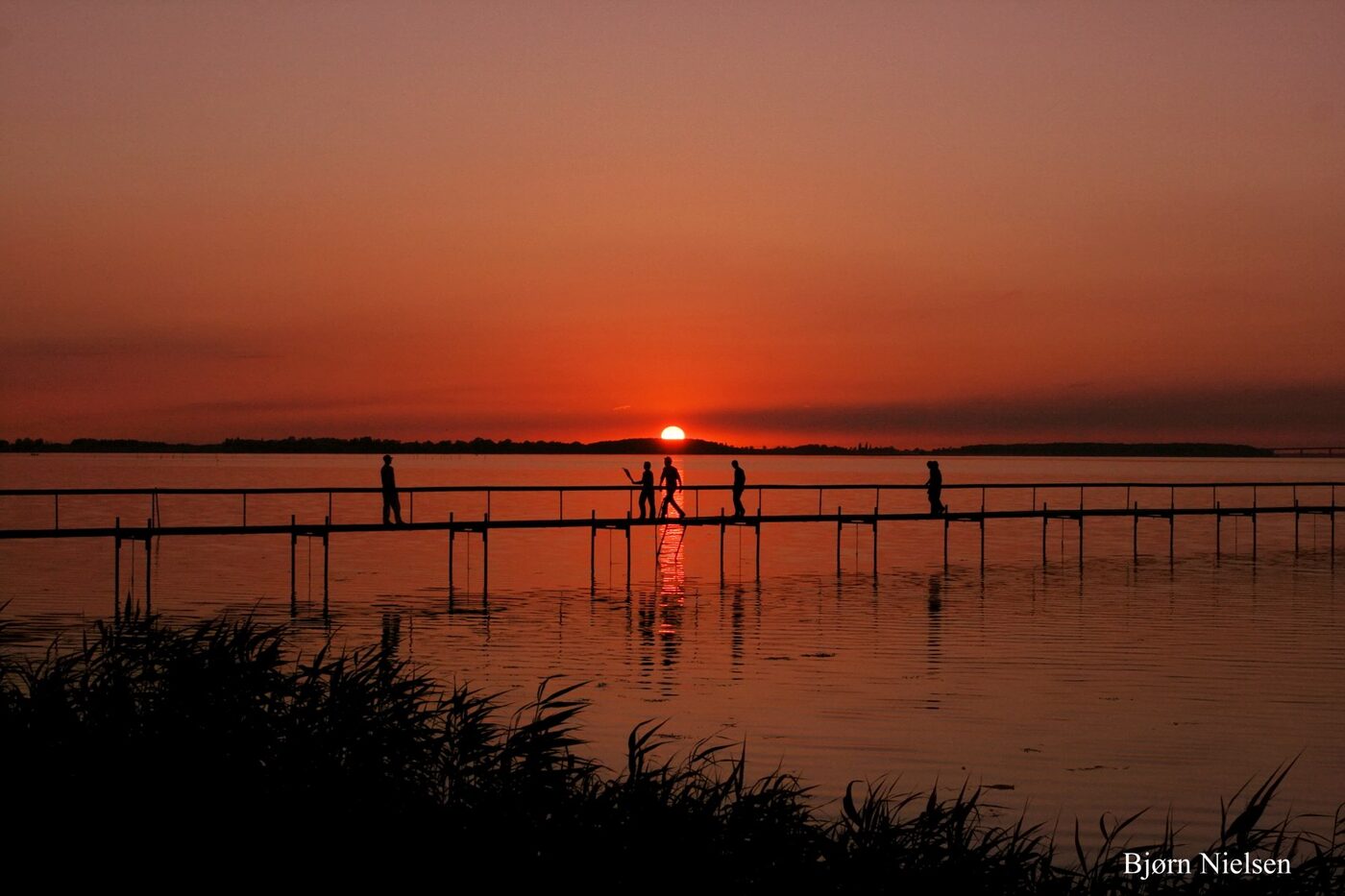 Mennesker på badebroen i solnedgang over Grønsund ved Stubbekøbing